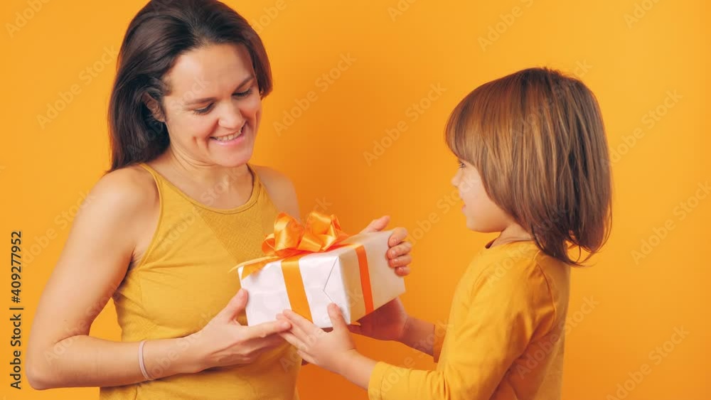 The girl gives his mother a box with a box gift on a yellow background. Mom's Concept Day, Birthday The girl gives his mother a box with a box gift on a yellow background. Mom's Concept Day, Birthday