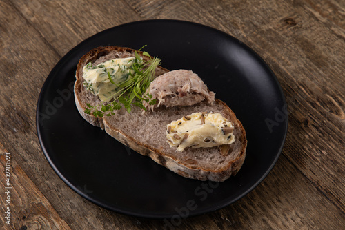 Sliced sour bread with three different bread spreads on black plate, wooden background  photo