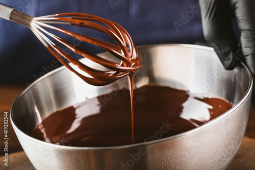 Melted dark chocolate drips from the whisk into a bowl of chocolate. Confectionery liquid chocolate.