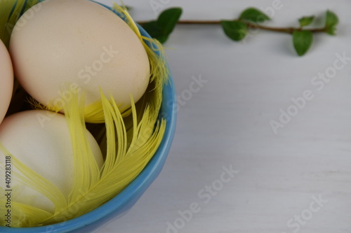 Easter eggs in blue bowl, yellow faethers, green twig onwhite wooden background photo