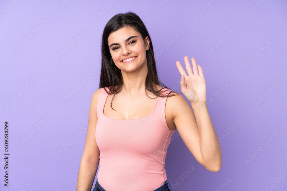 Young woman over isolated purple background saluting with hand with happy expression Young woman over isolated purple background saluting with hand with happy expression