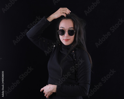 studio portrait of a beautiful girl in a black dress and sunglasses on a black background