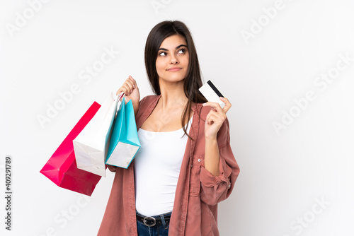 Young woman over isolated white background holding shopping bags and a credit card and thinking