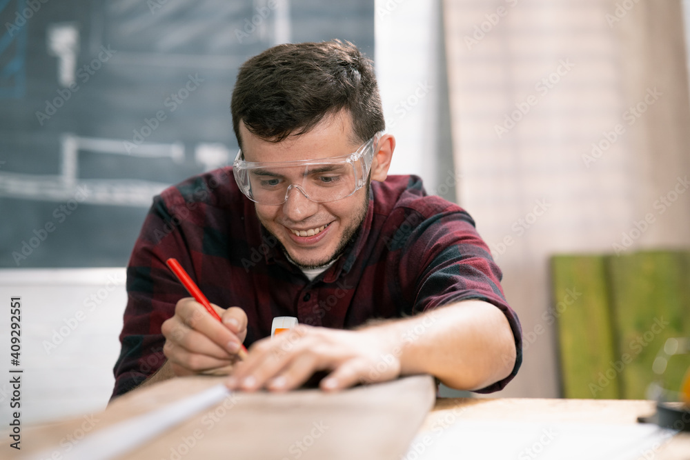 Carpenter at work. Man measures and marks wood board with metal ruler and pencil Carpenter at work. Man measures and marks wood board with metal ruler and pencil