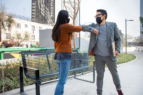 two young people greeting with the elbow on the street wearing protective masks