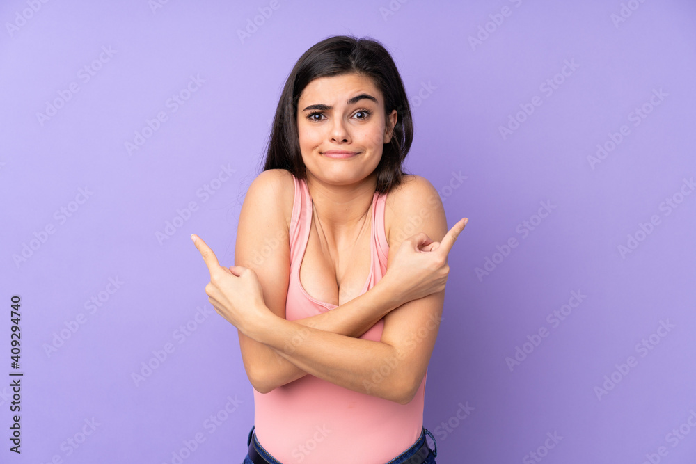 Young woman over isolated purple background pointing to the laterals having doubts