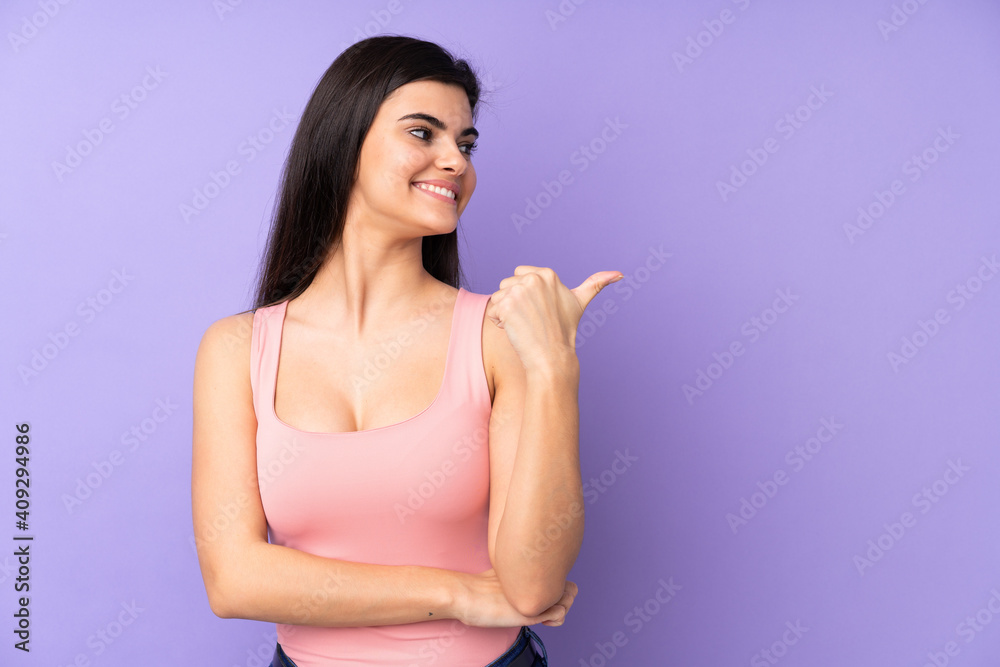 Young woman over isolated purple background pointing to the side to present a product Young woman over isolated purple background pointing to the side to present a product