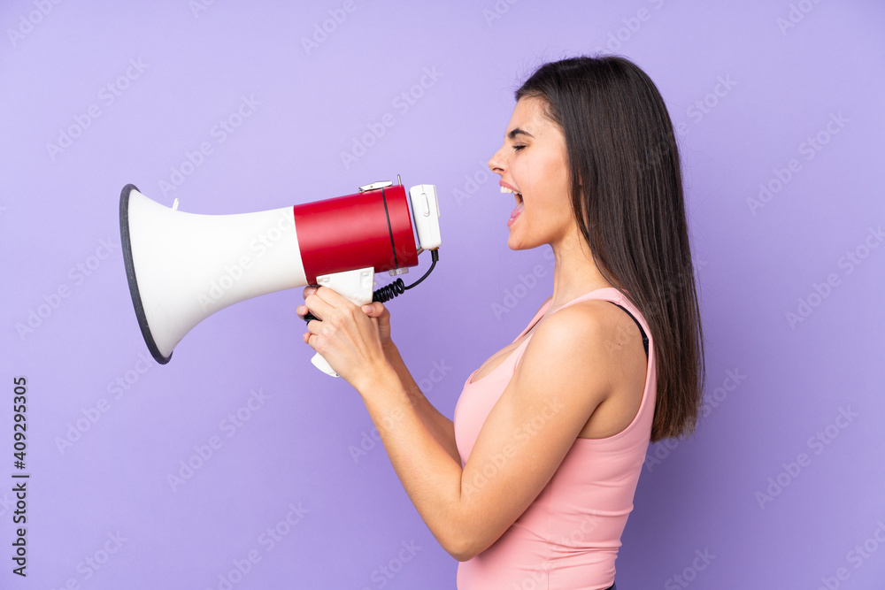 Young woman over isolated purple background shouting through a megaphone Young woman over isolated purple background shouting through a megaphone