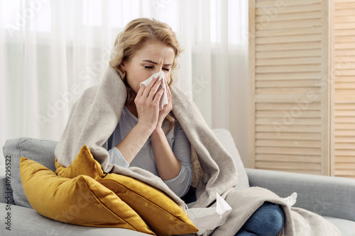 Ill woman with runny nose sneezes into a napkin photo
