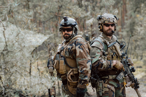 Portrait of a middle-aged bearded soldiers in a Woodland military uniform and helmet, with headphones on his head holding a rifle.