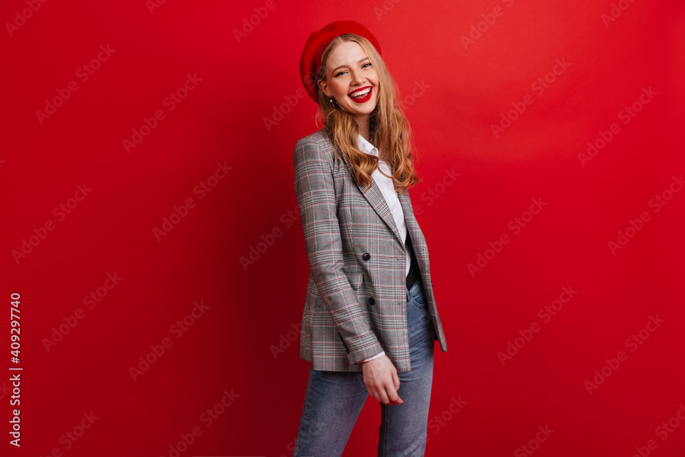 Stylish blonde woman in beret looking at camera. Studio shot of beautiful french girl in jacket standing on red background. Stylish blonde woman in beret looking at camera. Studio shot of beautiful french girl in jacket standing on red background.