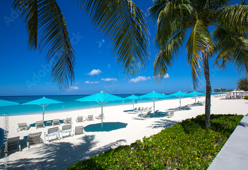 Grand Cayman Beach Deck Chairs Blue Umbrellas On Water s Edge.Caribbean  Grand Cayman  Seven Mile Beach  Cayman Islands  Palm Trees. Empty beach  No tourists