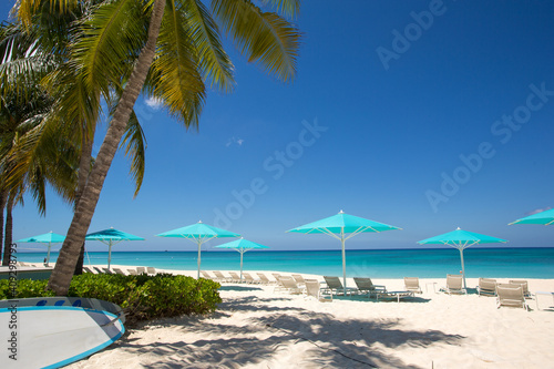 Grand Cayman Beach Deck Chairs Blue Umbrellas On Water s Edge.Caribbean  Grand Cayman  Seven Mile Beach  Cayman Islands  Palm Trees. Empty beach  No tourists