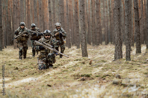 Fully Equipped Middle - Aged Soldiers Wearing Camouflage Uniform Attacking Enemy, They're in Shooting Ready Stance, Aiming Rifles. Military Operation in Action, Squad Standing in Dense Forest.