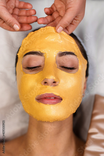 Procedure for skin care. Doctor in cosmetology office applies an yellow gold alginate mask to the face of young pretty woman. photo