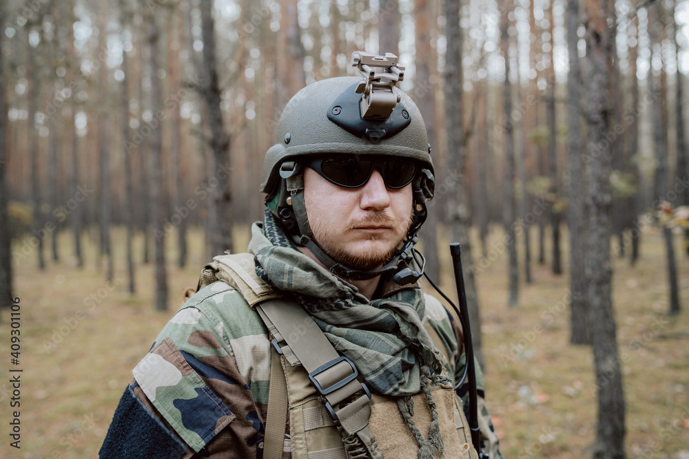Portrait of a middle-aged bearded soldier in a Woodland military uniform and helmet, with headphones on his head.