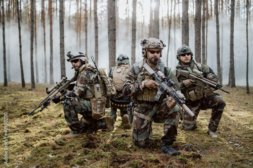 Fotobehang Four fully equipped, middle-aged soldiers in camouflage uniforms form a line, ready to fire, aiming with their rifles