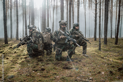 Four fully equipped, middle-aged soldiers in camouflage uniforms form a line, ready to fire, aiming with their rifles. A military operation in action, a unit standing in a dense forest. photo