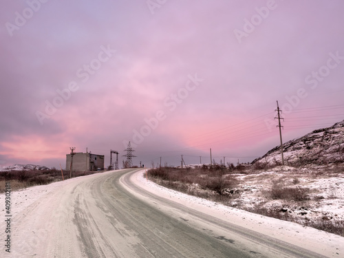 Snow turn on the road stretching away into the distance between the hills. The magical purple color of dawn.
