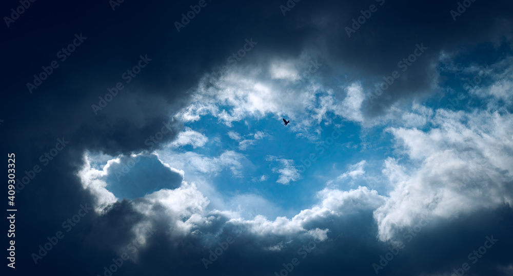 Dramatic cloud gathering, blue sky in the middle, a bird fly high up in the sky. Dramatic cloud gathering, blue sky in the middle, a bird fly high up in the sky.