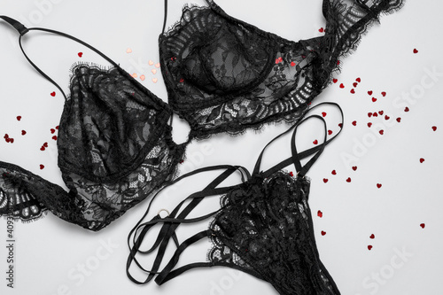 Lace sexy black womens underwear, red heart confetti on gray background flat lay top view copy space. Black lace lingerie. Fashion Concept. Women's bra, panties, erotic clothes. Lingerie advertising