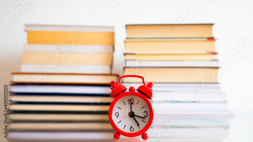 A red clock on a table and background of a notebooks.