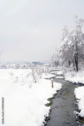 Stream or brook called Schaeflibach in winter flowing through village Urdorf in Switzerland. Both banks are covered with snow in extreme snowfall in January 2021.