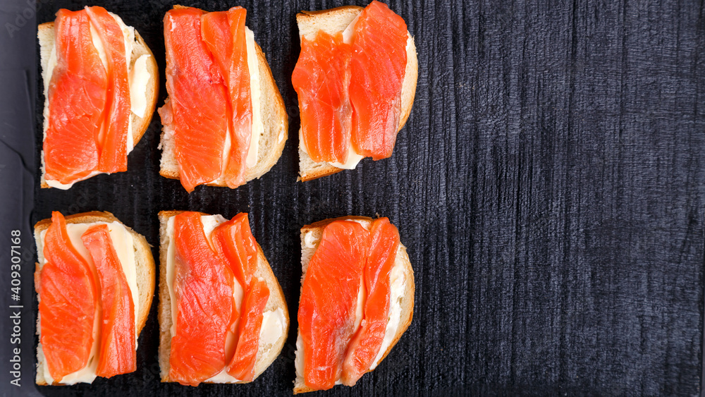 Bruschettes with butter and trout on a black board on a gray concrete background copy space. Bruschettes with butter and trout on a black board on a gray concrete background copy space.
