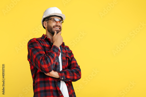 Confident bearded engineer or constructor man in plaid shirt thinking over yellow background. Looking away.