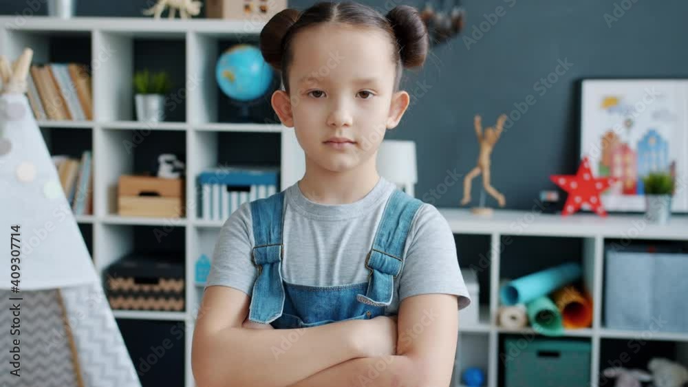Slow motion portrait of serious beautiful child standing at home alone with arms crossed and looking at camera. Character and childhood concept. Slow motion portrait of serious beautiful child standing at home alone with arms crossed and looking at camera. Character and childhood concept.