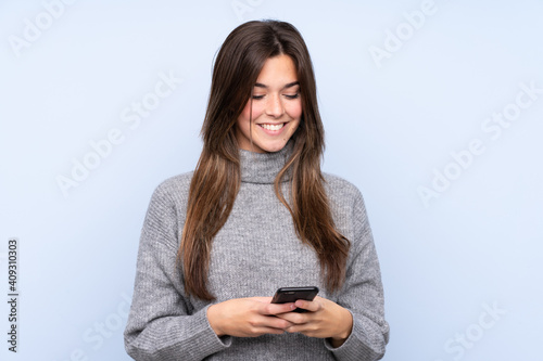 Teenager Brazilian girl over isolated blue background sending a message with the mobile