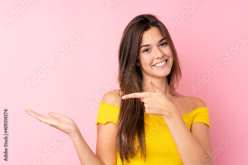 Teenager Brazilian girl over isolated pink background holding copyspace imaginary on the palm to insert an ad