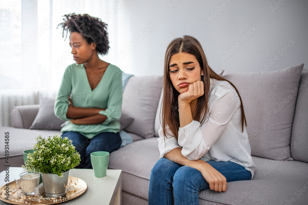 Obraz premium Unhappy young female friends not talking after argument at home on the couch. Two female friends sitting on sofa and arguing. Unhappy friends not talking after argument on the couch