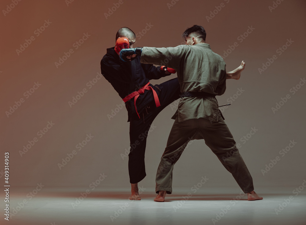 Wrestling of two fighting males in kimono and boxing gloves in red light in studio, martial arts, mixed fight concept