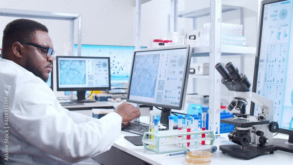 Professional African-American scientist is working on a vaccine in a modern scientific research laboratory. Genetic engineer workplace. Futuristic technology and science concept. Professional African-American scientist is working on a vaccine in a modern scientific research laboratory. Genetic engineer workplace. Futuristic technology and science concept.