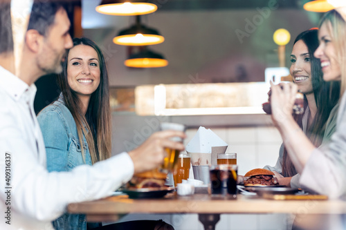 Attractive young friends group eating burgers while talking and having fun in the restaurant.