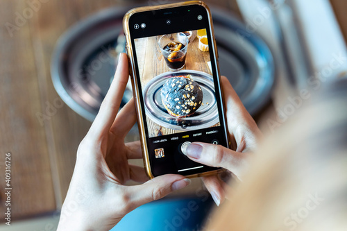 Young woman's hands photographing tempting burger on smartphone to upload on social media in a restaurant.