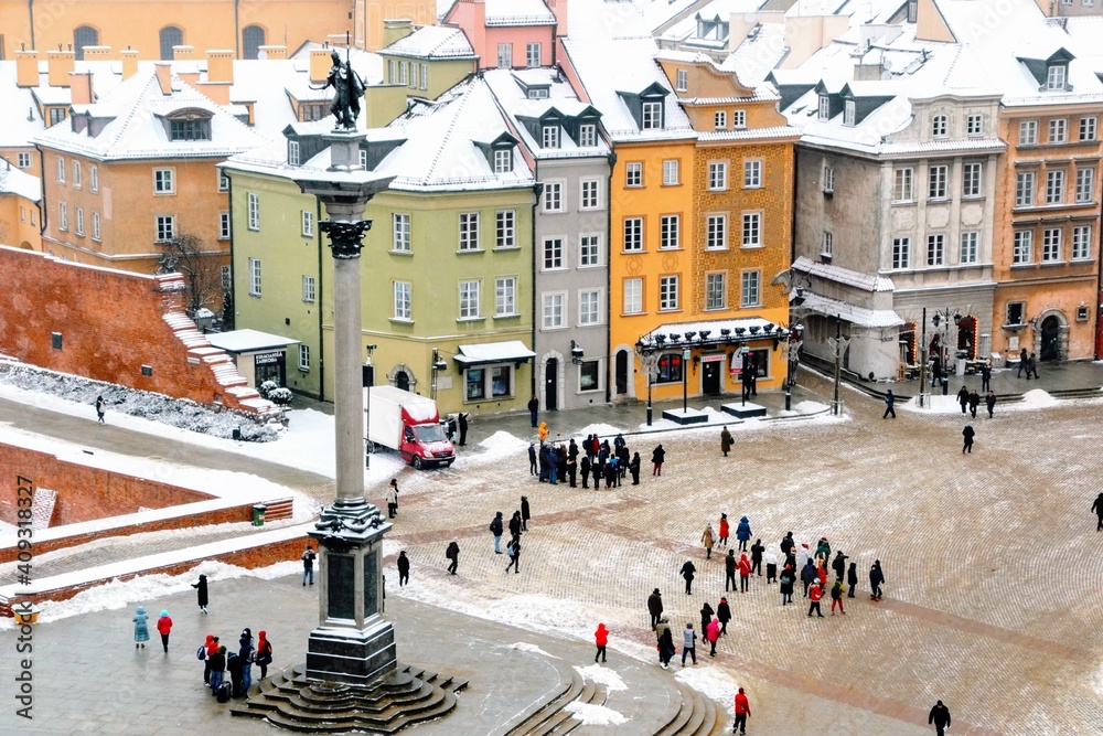 Winter at Castle Square in Warsaw - aerial view from the bell tower of the  St. Anne church. Snow on the roofs of Old Town buildings. Tourists at the Castle Square