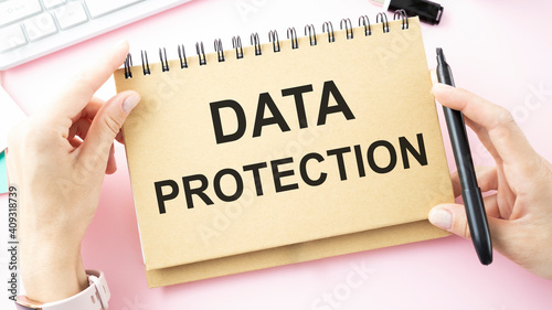 Notepad with the words DATA PROTECTION in the hands of an employee against the background of the office table.