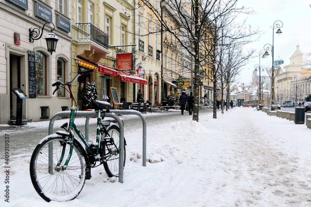 Green bike parked in the snow at cold winter day. Krakowskie Przedmiescie (literally: Krakow suburb) street - one of the best known streets of Warsaw. Warsaw, Poland 
