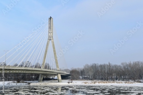 Swietokrzyski Bridge over Vistula river, Warsaw, Poland. Modern, cable-stayed bridge with single tower and cables attached supporting the deck. Winter time, fragments of ice float on the river