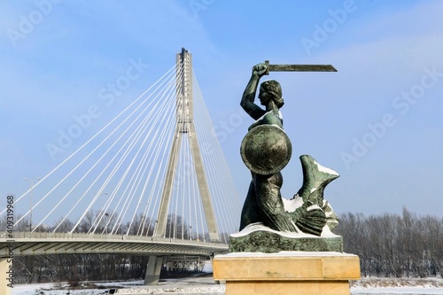 Statue of Mermaid (Polish: Warszawska Syrenka) symbol of Warsaw by the Vistula river on the background of Swietokrzyski Bridge. Winter time in Warsaw, Poland. 