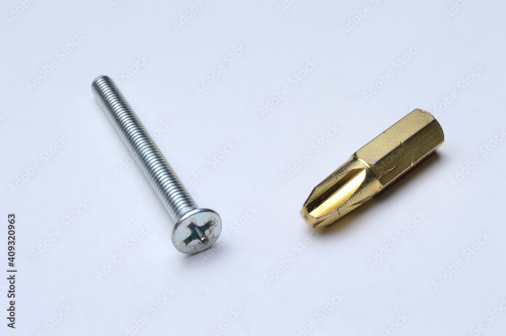a gold-colored bit and a bolt lie on a light background close-up. a gold-colored bit and a bolt lie on a light background close-up.