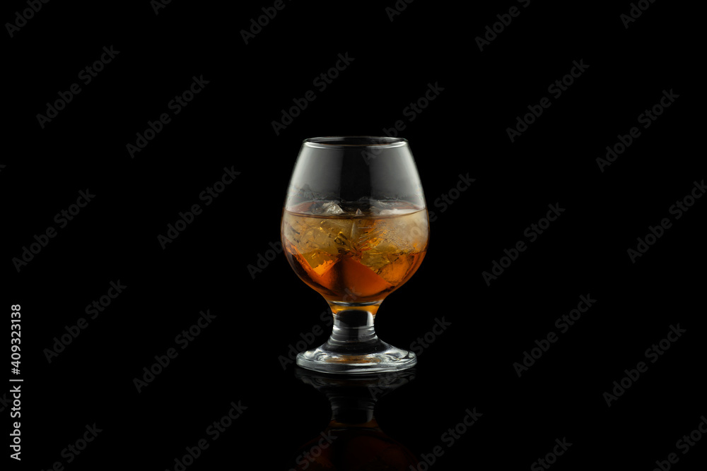 Glass of cognac with ice isolated on black background.