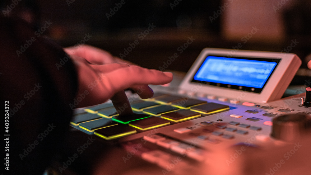 The hands of an artist creating music with his drum machines under red light.