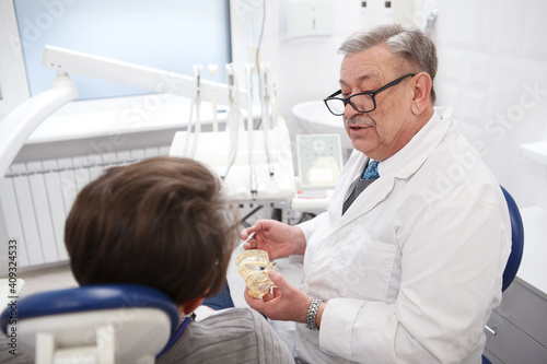 Elderly male dentist working at his clinic  talking to the patient