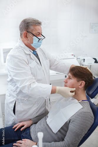 Vertical shot of a professional dentist wearing medical face mask  examining lymphatic nods of patient prior to dental treatment