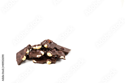 Pieces of dark chocolate with whole hazelnuts on a white background