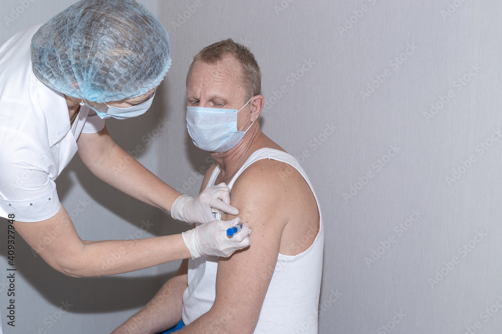 Vaccination against coronavirus. A nurse puts the shot in the shoulder of a mature man wearing a protective mask. Immunization of the population.