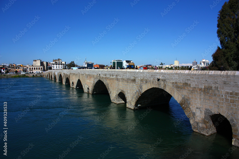 Adana, Turkey – March 25, 2011: Day in Adana, Turkey. View of old bridge that made of Stones. People walk on bridge. Old bridge made of stone, is standing on  the river of Adana that is the fifth bigg
